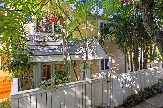 Front view of a two-story house with a white picket fence and surrounded by trees.