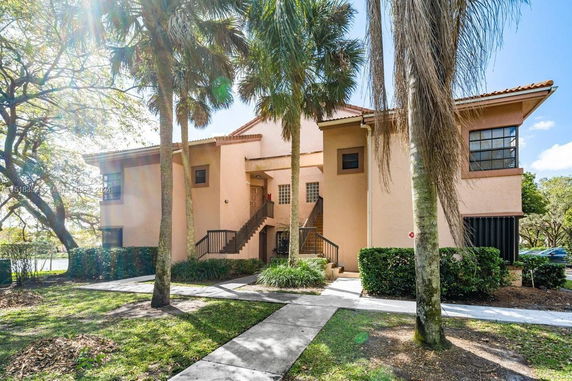 Front view of a two-story residential building with external staircases and palm trees in front.