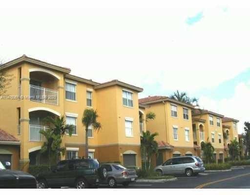 Front view of a multi-story residential building with balconies and a street parking area.