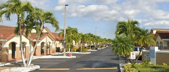 Front view of a series of single-story houses with red-tiled roofs and palm trees lining the street.