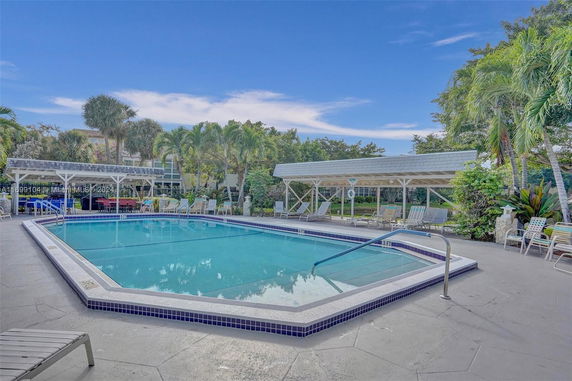View of an outdoor swimming pool with surrounding lounge chairs and a covered seating area.