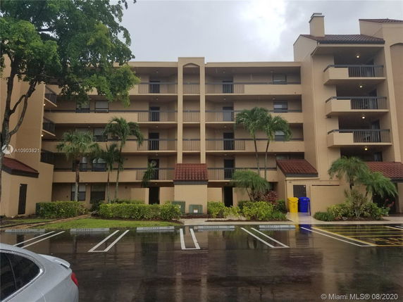 Front view of a multi-story apartment building with balconies and a parking area in front.