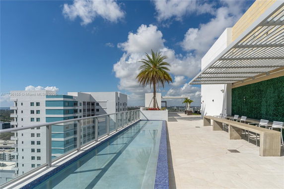 Rooftop view of a modern building with a swimming pool, palm trees, and a seating area under a trellis.