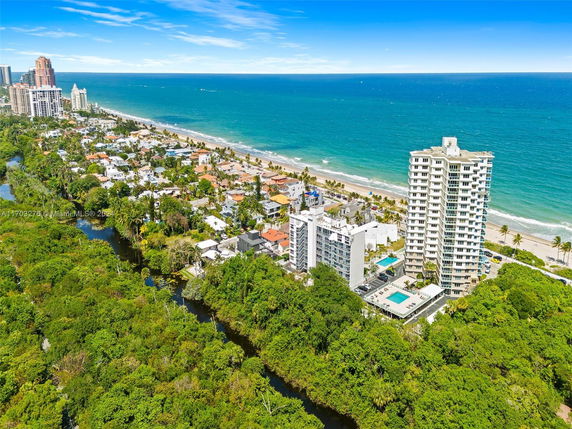 Aerial view of a coastal area with a high-rise building and surrounding residential houses near the ocean.