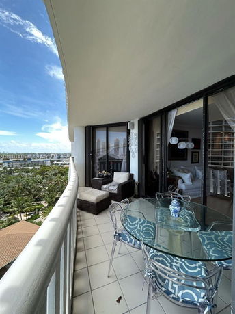 Balcony with outdoor seating and glass table, view overlooking trees and buildings.