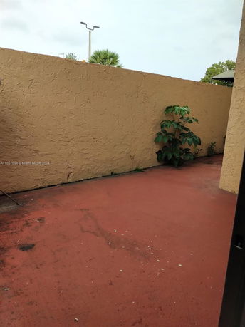 Outdoor area with red flooring and beige stucco walls.