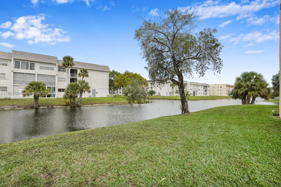 Apartment buildings near a water body with a grassy area and trees.