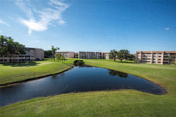 View of apartment buildings with a pond and grassy area in the foreground.