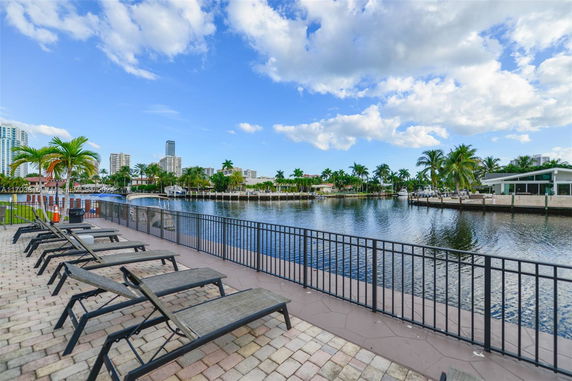 View of waterfront area with lounge chairs and buildings in the background.