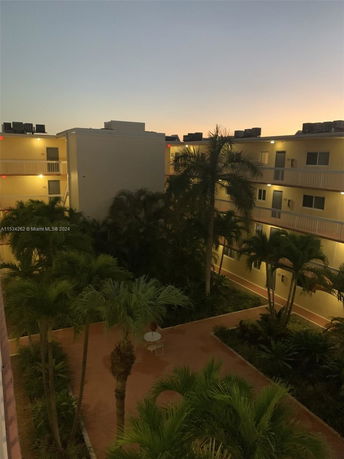 View of an apartment complex with multiple levels and balconies, surrounded by palm trees at dusk.
