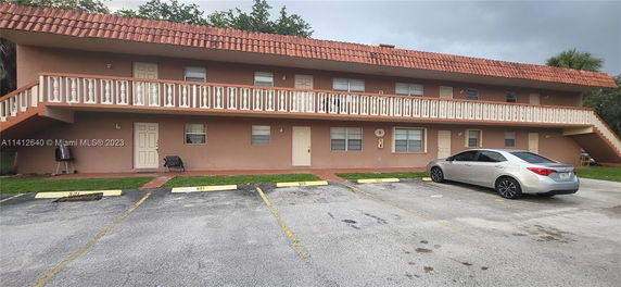 Front view of a two-story building with a balcony and parking area.