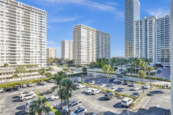 Outdoor parking area with multiple cars and high-rise buildings surrounding the area.