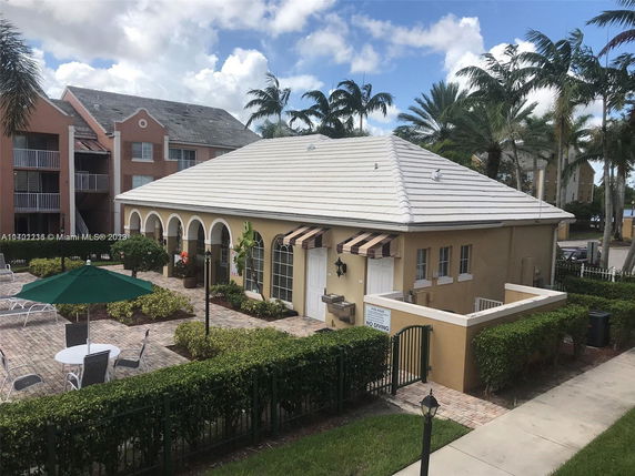 Front view of a building with arched windows and a white tiled roof, situated near a patio area with tables and chairs.