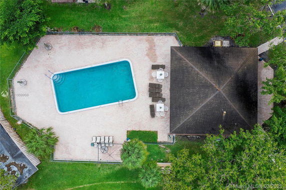 Aerial view of a rectangular swimming pool next to a building with a tiled deck area.