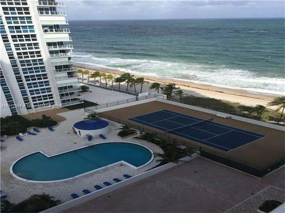 High-rise building with a view of a swimming pool and tennis court near the beach.