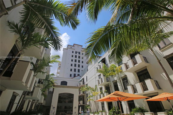 View of multi-story buildings with balconies and palm trees in a courtyard setting.