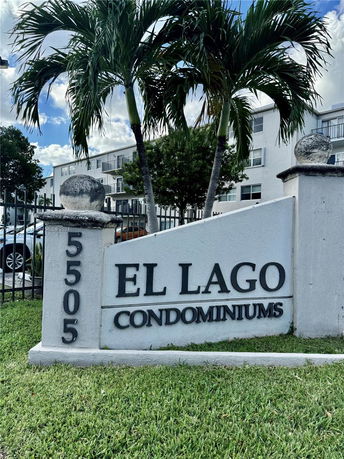 Front view of a condominium building with palm trees and a sign reading 'El Lago Condominiums'.