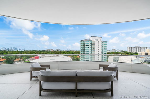 Panoramic view from a balcony with outdoor seating, facing modern buildings and cityscape.