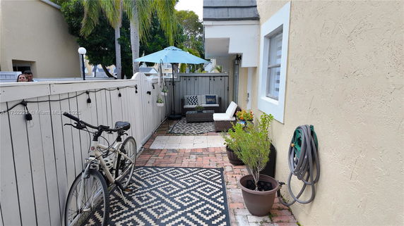 Outdoor area with a decorative rug, bicycle, seating, potted plants, and a bright umbrella.