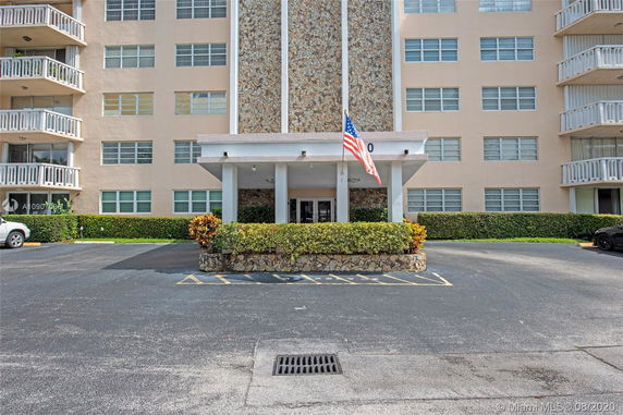 Front view of a multi-story building with a central stone facade and an entrance under a covered walkway.