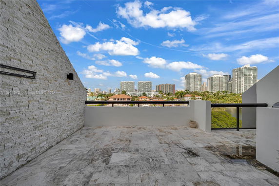 Rooftop with stone tile flooring and railing, overlooking a view of distant high-rise buildings.