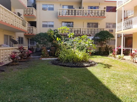 View of apartment building with balconies and a garden in the foreground.