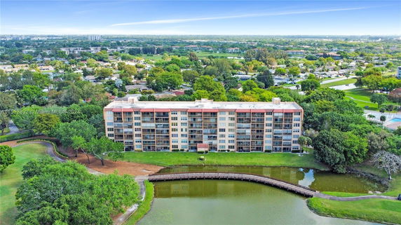 Aerial view of a multi-story residential building surrounded by greenery and a small body of water.