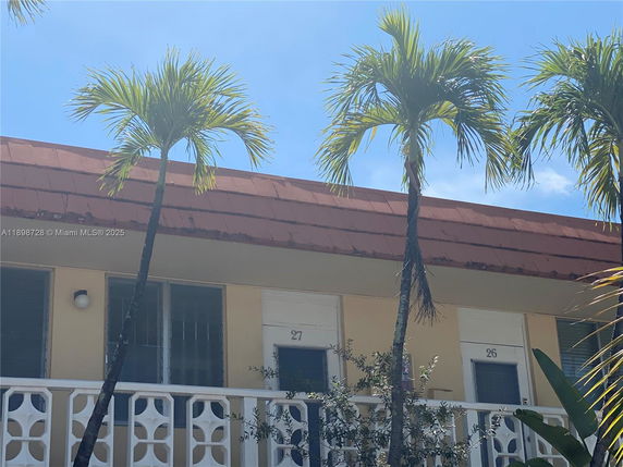 Front view of a one-story building with a distinct red roof and number-marked entrances, surrounded by palm trees.