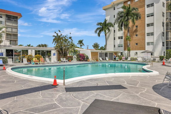 View of a swimming pool area with surrounding apartment buildings and palm trees.