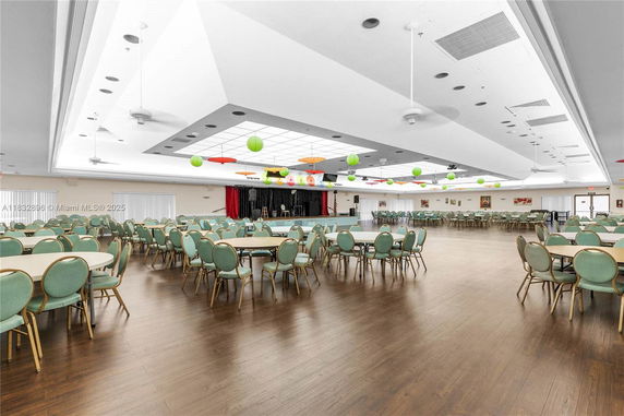 Large indoor club house area with round tables and chairs, stage, and ceiling decorations.