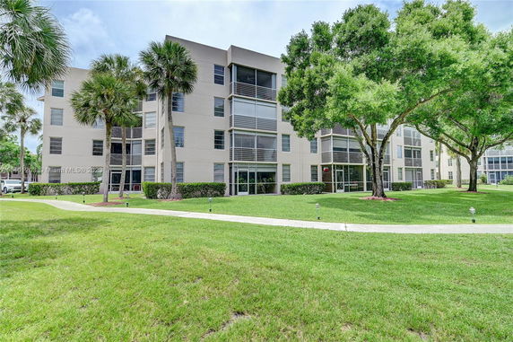Front view of a multi-story residential building with large windows and surrounding greenery.
