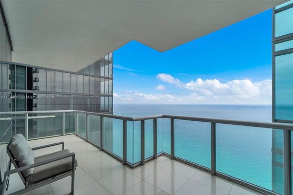 Balcony with glass railing overlooking the sea with a view of neighboring building.