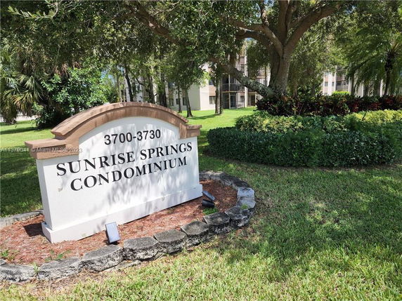 Front view of a multi-story condominium building with a large sign reading 'Sunrise Springs Condominium'.
