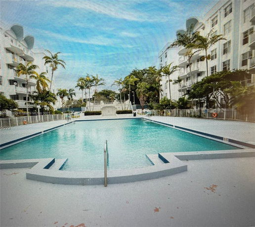 View of a pool area surrounded by multi-story buildings and palm trees.