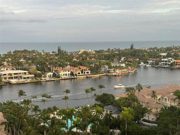 Panoramic view of a coastal area with waterfront properties, palm trees, and a body of water with boats.