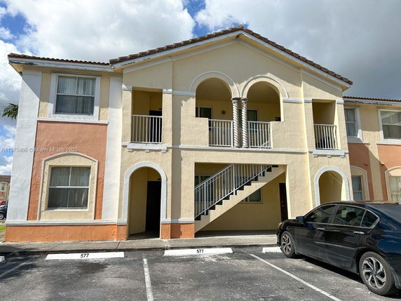 Front view of a two-story building with arched balconies and visible parking area.