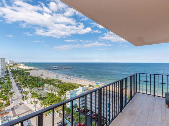 Balcony view overlooking a beach and ocean with a boardwalk and surrounding buildings.
