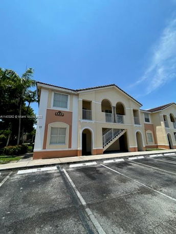 Front view of a two-story residential building with arched balconies and a parking area in the foreground.