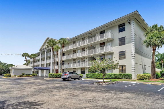 Front view of a four-story apartment building with balconies and a parking area.