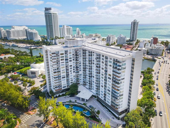 Aerial view of a high-rise apartment building near the ocean, surrounded by other tall buildings.
