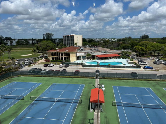 View of a residential area with a swimming pool, tennis courts, and surrounding greenery.