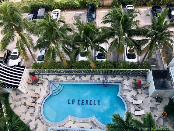View of a rooftop with a swimming pool, deck chairs, and palm trees.