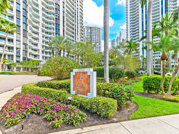 Front view of a tall residential tower with balconies and landscaped entrance.