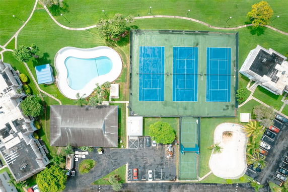 Aerial view of a recreational area with tennis courts, a swimming pool, and surrounding grassy areas.