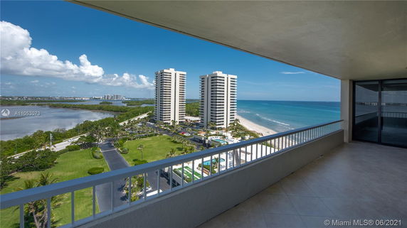 View from a high-rise balcony overlooking the ocean and two tall buildings.