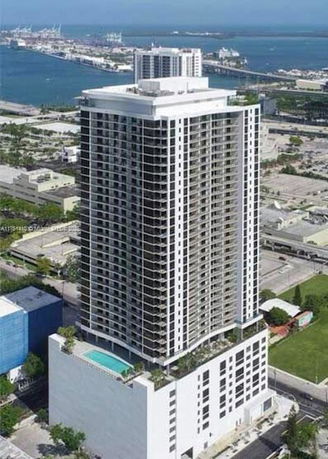 Front view of a high-rise residential building with balconies and a swimming pool on the lower rooftop terrace.