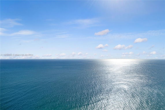 Wide view of the ocean with blue sky and scattered clouds.
