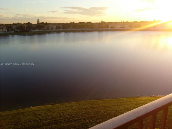 View of a large water body with grassy shore and distant horizon during sunset.