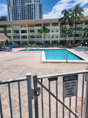 Outdoor swimming pool area with surrounding deck and a gated entrance in front of an apartment building.