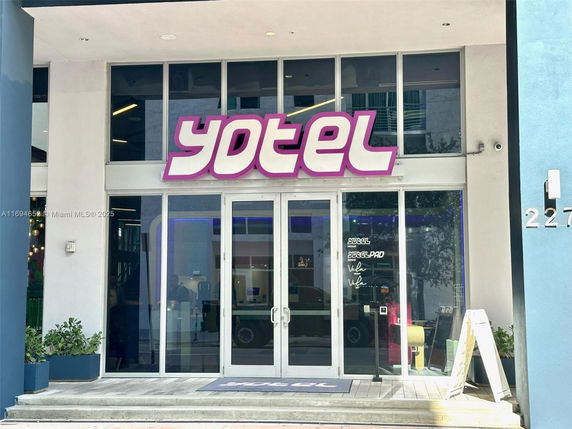 Front view of a modern building entrance with large glass doors and a prominent sign above.